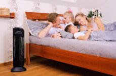 Purificatore d'aria Ionic-CARE in camera da letto vedle postele ve které si povídají matka, otec a jejich 2 malé děti, colore nero