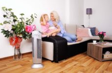 Purificatore d'aria Ionic-CARE in soggiorno accanto al divano dove una giovane mamma si rilassa con la figlia, colore argento
